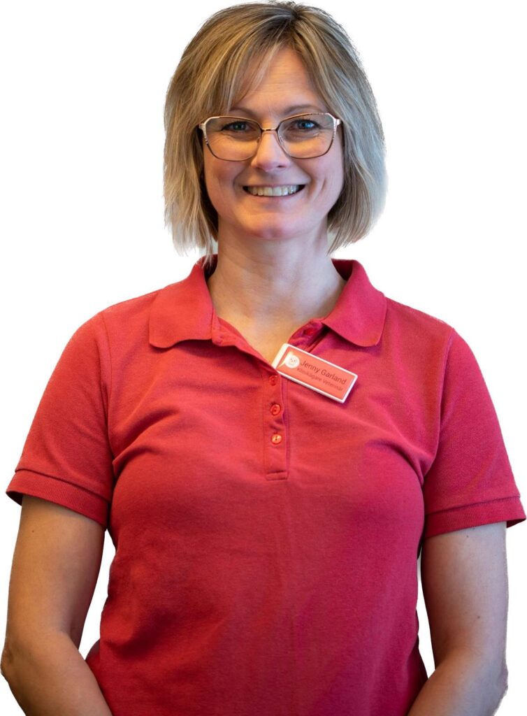 En bild på Jenny Garland. Bilden är beskuren vid midjan. Hon har guldfärgade glasögon och frisyr med håret ner till halva halsen. Hon är iklädd en röd tenniströja och hon har en namnbricka på tröjan.